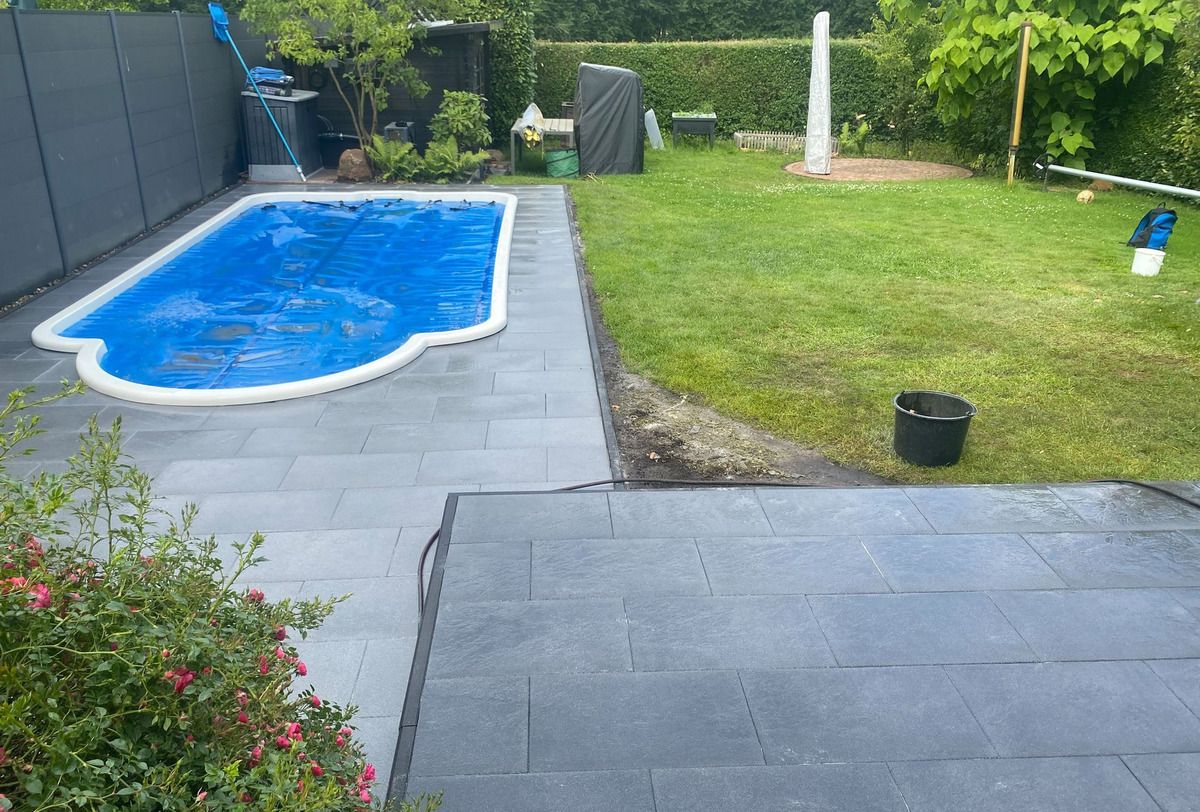 Eingelassener Pool mit blauer Abdeckplane, ringsum Plattenbelag und Rasen