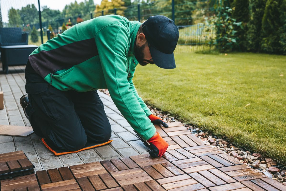 Handwerker verlegt quadratische Holzfliesen auf einer bestehenden Steinterrasse