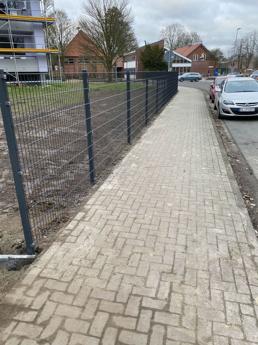 Neu gesetzter Zaun entlang eines gepflasterten Gehwegs